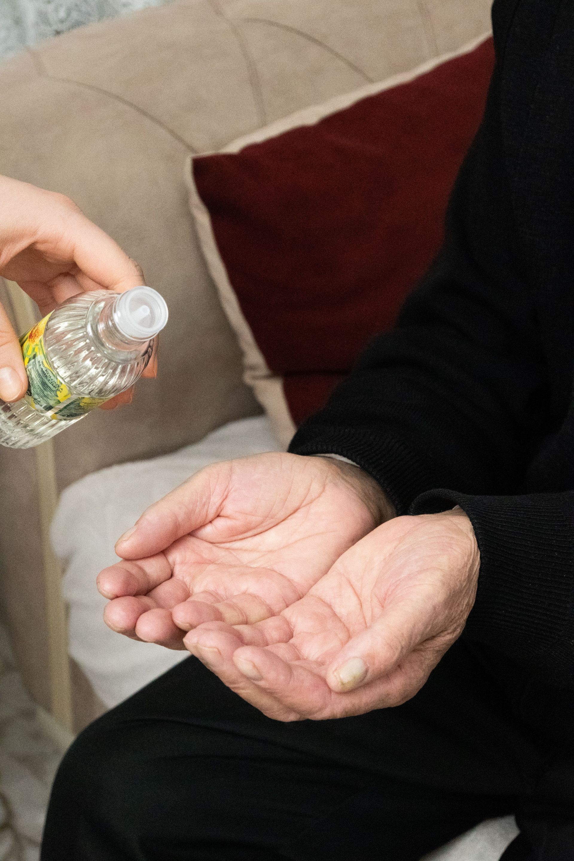 A person applying hand sanitizer to the hands of a senior adult indoors.